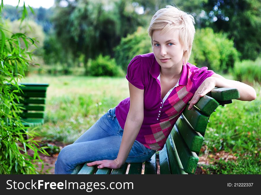 Attractive Blonde Woman Sitting On Bench In Park