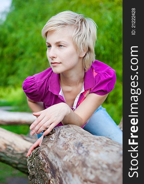 Beautiful young blonde woman outdoors in the park sitting on the tree branch. Beautiful young blonde woman outdoors in the park sitting on the tree branch