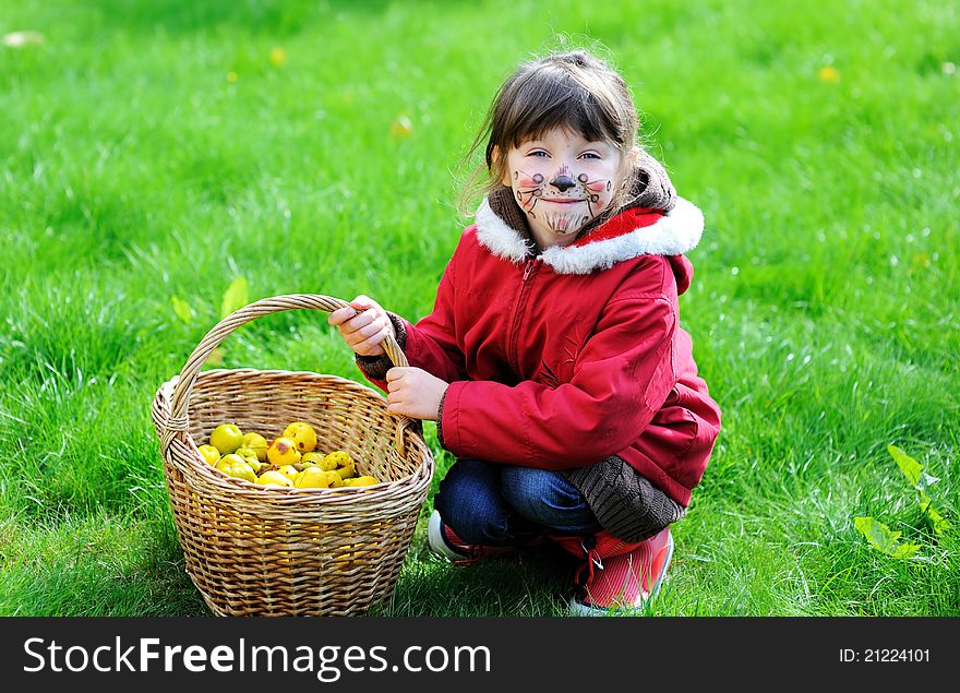 Cute little girl with face painted sitting outdoors with garden basket filled up with Japan quince. Cute little girl with face painted sitting outdoors with garden basket filled up with Japan quince