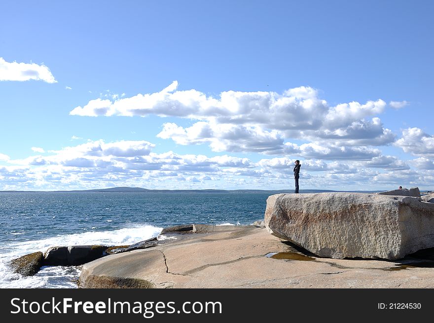 A girl is standing on a rock at the Peggy's Cove, Nova Scotia, Canada. The blue ocean water, blue sky, white cloud and the beautiful girl composed a nice view. A girl is standing on a rock at the Peggy's Cove, Nova Scotia, Canada. The blue ocean water, blue sky, white cloud and the beautiful girl composed a nice view.