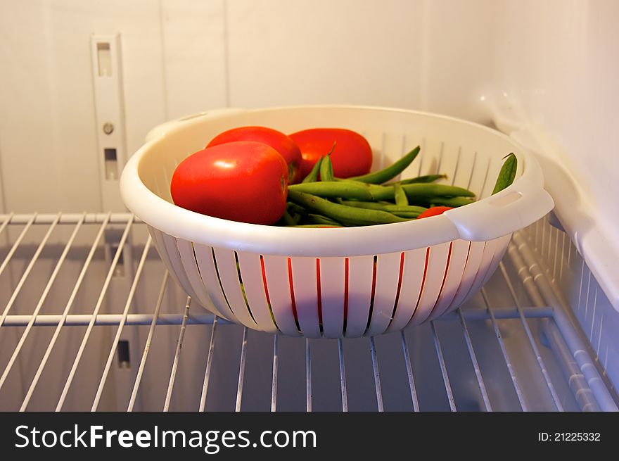 A colander full of garden fresh tomatoes and green beans on shelf in refrigerator, lit by refrigerator light. A colander full of garden fresh tomatoes and green beans on shelf in refrigerator, lit by refrigerator light.