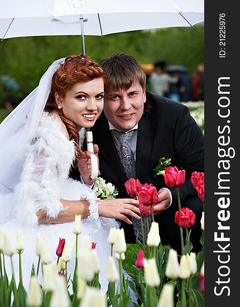 Happy bride and groom with umbrella at wedding walk in park surrounded by flowers. Happy bride and groom with umbrella at wedding walk in park surrounded by flowers