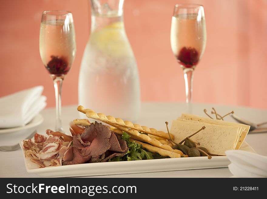 Entree dish with pastry crackers,roast beef,prosciutto,salami and rocket with 2 glasses and a bottle of water on the background. Entree dish with pastry crackers,roast beef,prosciutto,salami and rocket with 2 glasses and a bottle of water on the background
