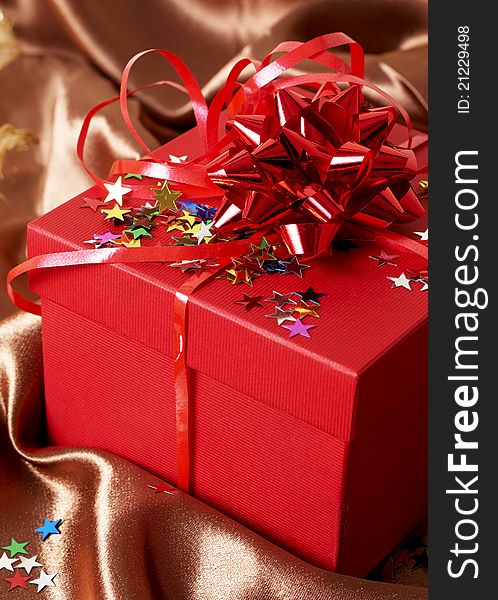 Red gift box with bows and stars on golden silk background