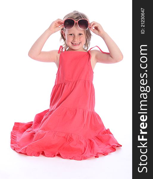 Cute blonde six year old primary school girl wearing coral pink dress kneeling on the floor having fun with sunglasses. Cute blonde six year old primary school girl wearing coral pink dress kneeling on the floor having fun with sunglasses.