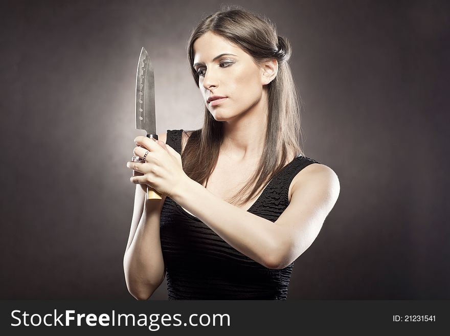 Beautiful brunette woman looks threatening and a bit seductive with a knife in her hands. Beautiful brunette woman looks threatening and a bit seductive with a knife in her hands.
