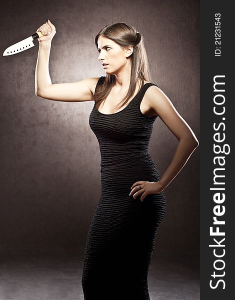 Beautiful brunette dressed in a black dress on a brown background is holding a knife in a threatening way. Beautiful brunette dressed in a black dress on a brown background is holding a knife in a threatening way.