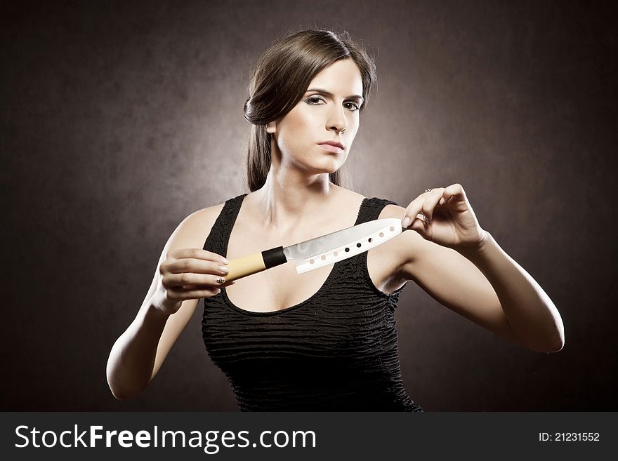 Beautiful brunette dressed in a black dress on a brown background is holding a knife in a threatening way. Beautiful brunette dressed in a black dress on a brown background is holding a knife in a threatening way.