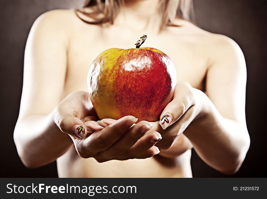 Beautiful topless woman is holding a red and yellow beautiful apple in front of her breasts. The focus is on the apple. Beautiful topless woman is holding a red and yellow beautiful apple in front of her breasts. The focus is on the apple.