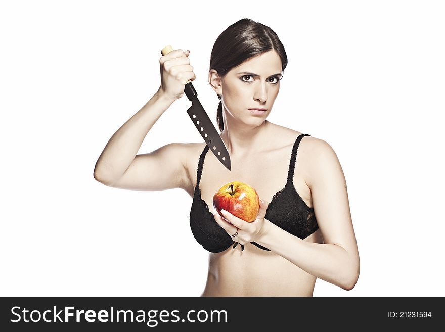 Dangerous looking woman, in a black lace bra is trying to stab a beautiful apple, on a white background. Dangerous looking woman, in a black lace bra is trying to stab a beautiful apple, on a white background.