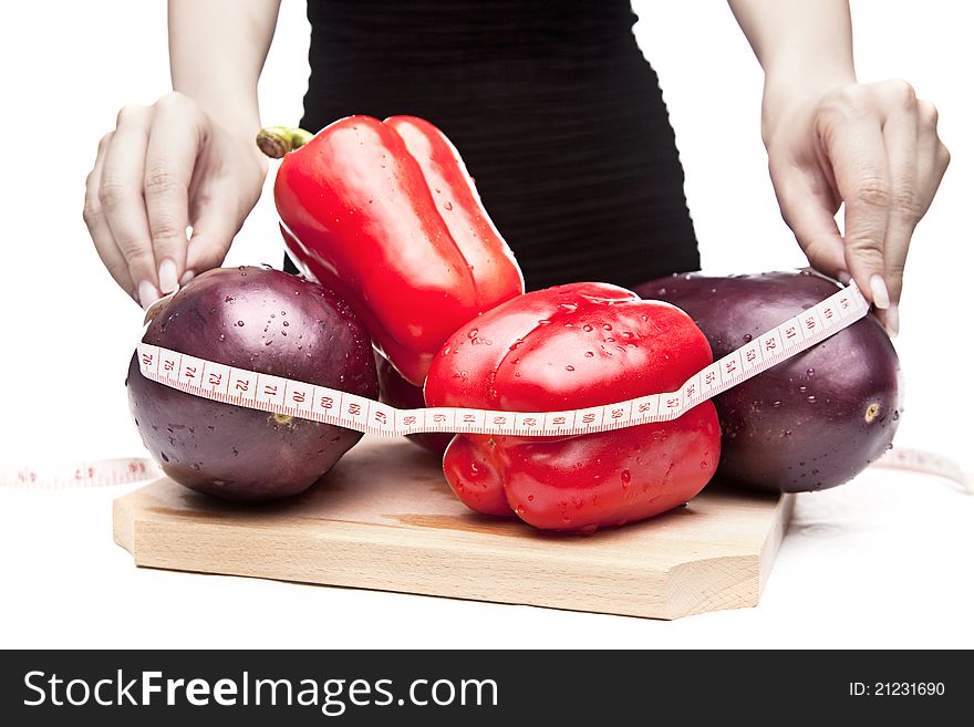 Woman in a black dress is measuring red peppers and eggplants with a centimeter on a white background. Woman in a black dress is measuring red peppers and eggplants with a centimeter on a white background.