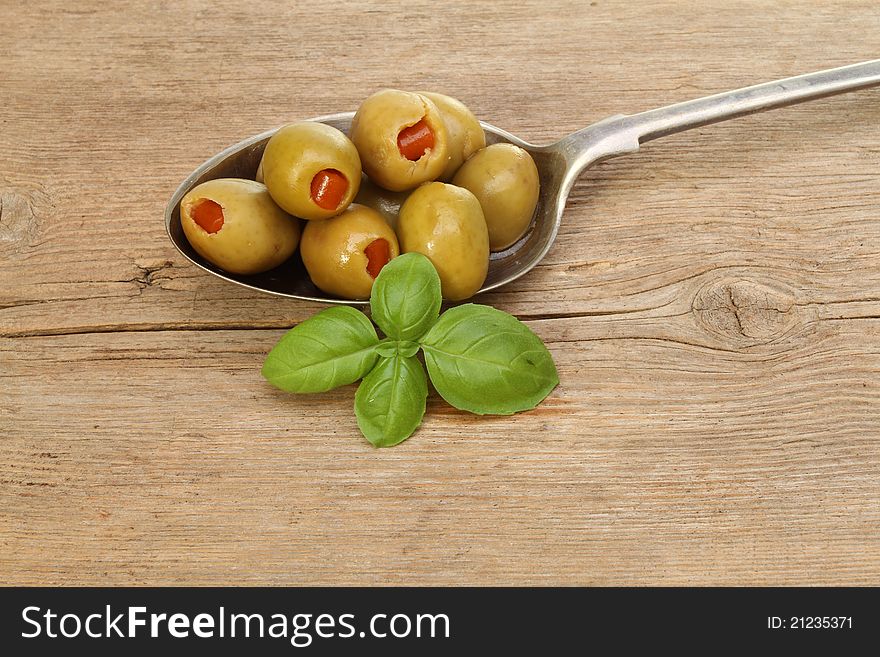 Stuffed olives in silver spoon with a sprig of basil on old rustic wood. Stuffed olives in silver spoon with a sprig of basil on old rustic wood