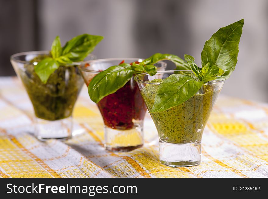 Three kind of pestos in small glasses with few leaves of basil