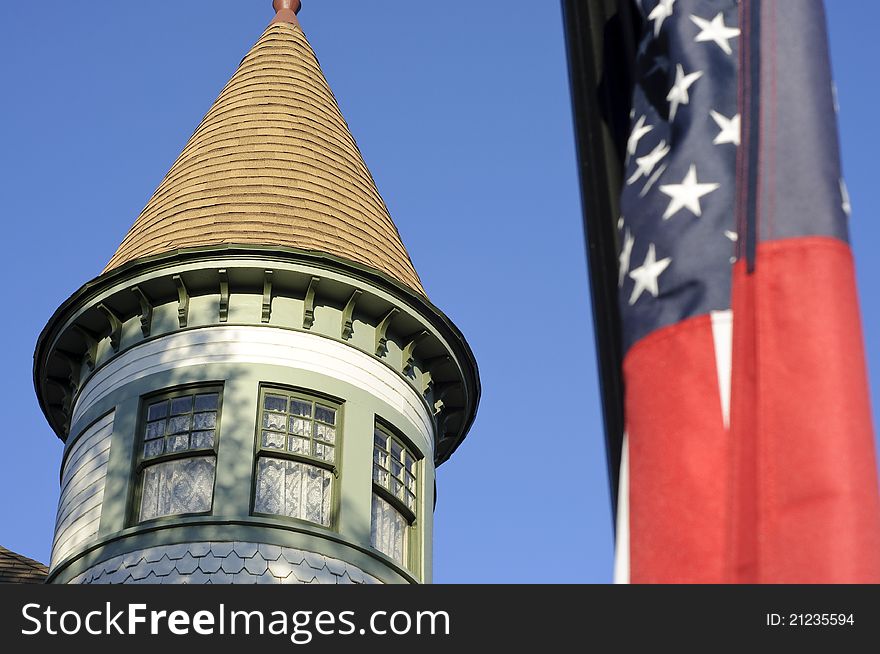 The top of an old Victoria style house in Anaheim with a US flag in the foreground slightly blurred. The top of an old Victoria style house in Anaheim with a US flag in the foreground slightly blurred.