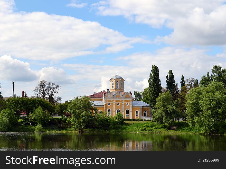 Church on the riverbank with a blue sky and green trees.