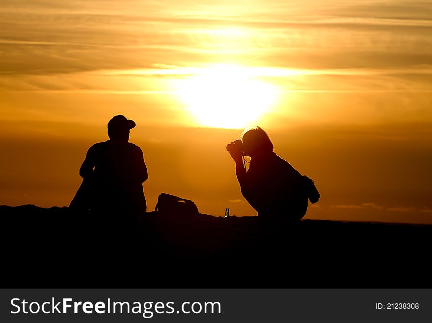 Silhouette of female photographer at sunset photographing friend