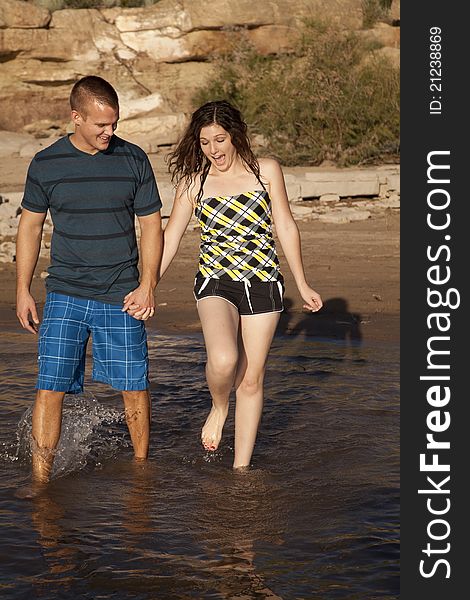 A couple holding hands and walking in the water together, the girl thinks it is cold. A couple holding hands and walking in the water together, the girl thinks it is cold.