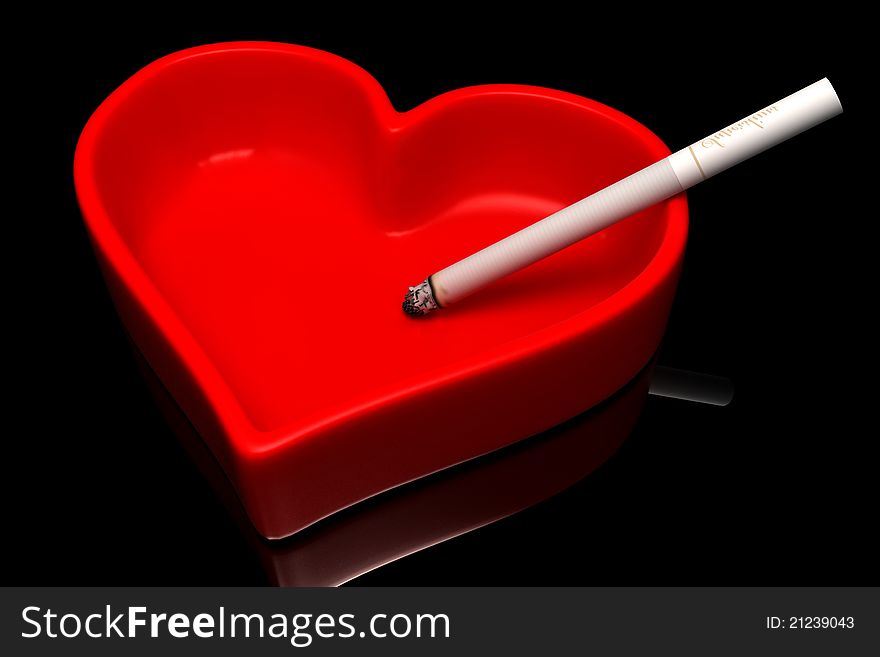 Red ashtray with a cigarette on a black background