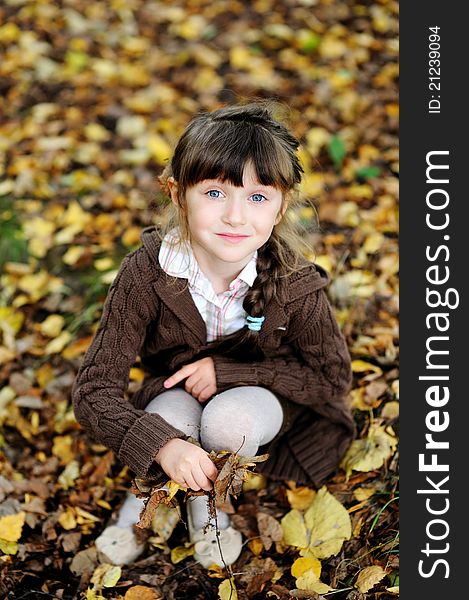 Cute child girl sitting on carpet of autumn leaves