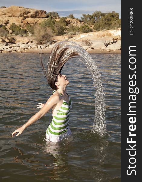 A woman standing waist deep in the water fliping her hair to make a water rainbow. A woman standing waist deep in the water fliping her hair to make a water rainbow.