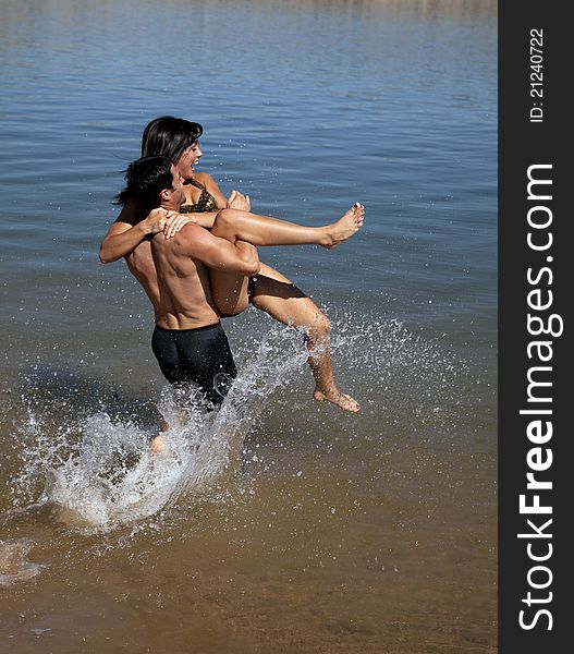 A men carrying his girlfriend out to the water kicking and screaming. A men carrying his girlfriend out to the water kicking and screaming.