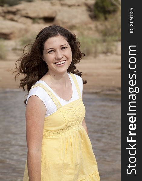 A woman standing by the water in her yellow dress with a smile on her face. A woman standing by the water in her yellow dress with a smile on her face.