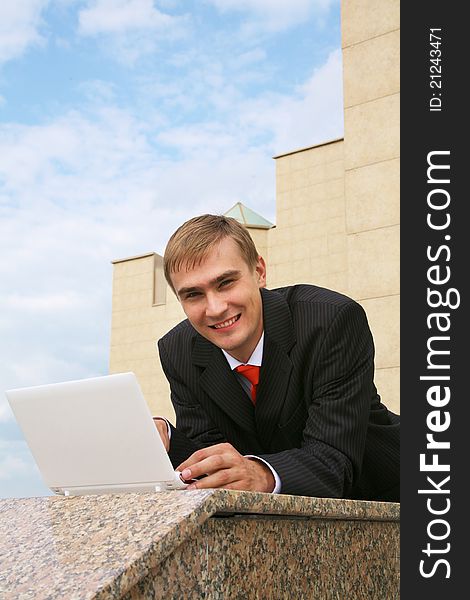 Portrait of confident businessman with laptop lying near the building. Portrait of confident businessman with laptop lying near the building