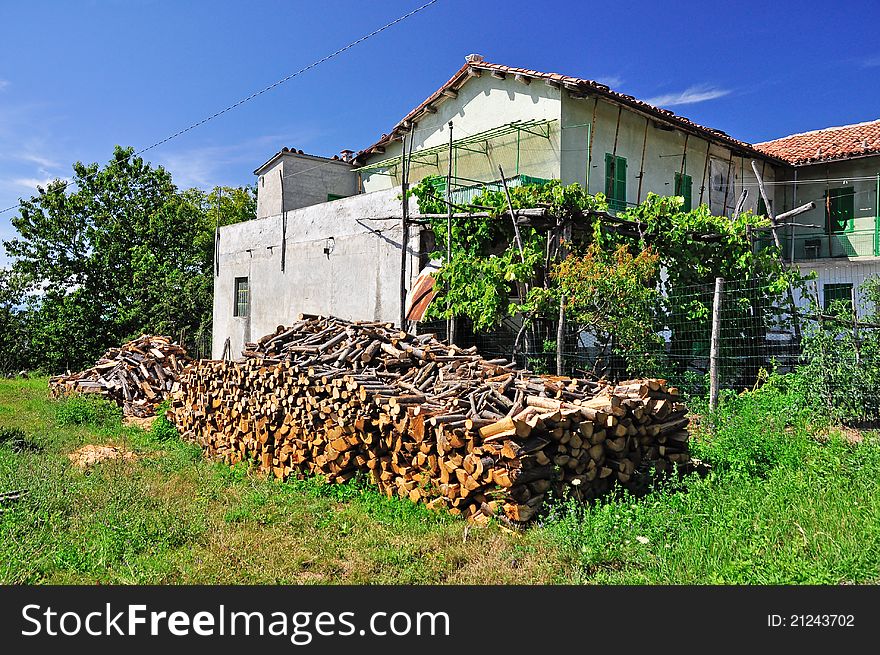 House in countryside with the chopped firewood logs stacked in a pile on the foreground.