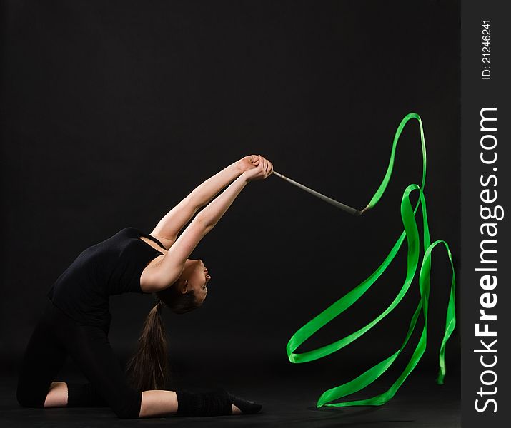 Attractive woman dancing with green ribbon against dark background. Attractive woman dancing with green ribbon against dark background