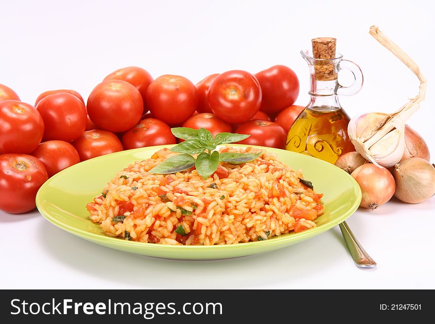 Risotto with tomatoes on a green plate decorated with basil with fresh tomatoes, onions, garlic and olive oil on white background