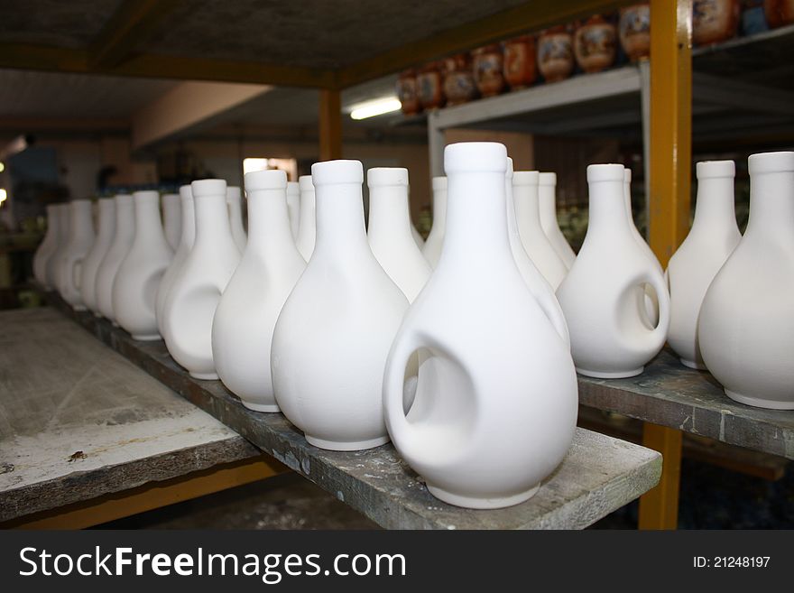 A considerable quantity of white ceramic pots which stand on a wooden table abreast