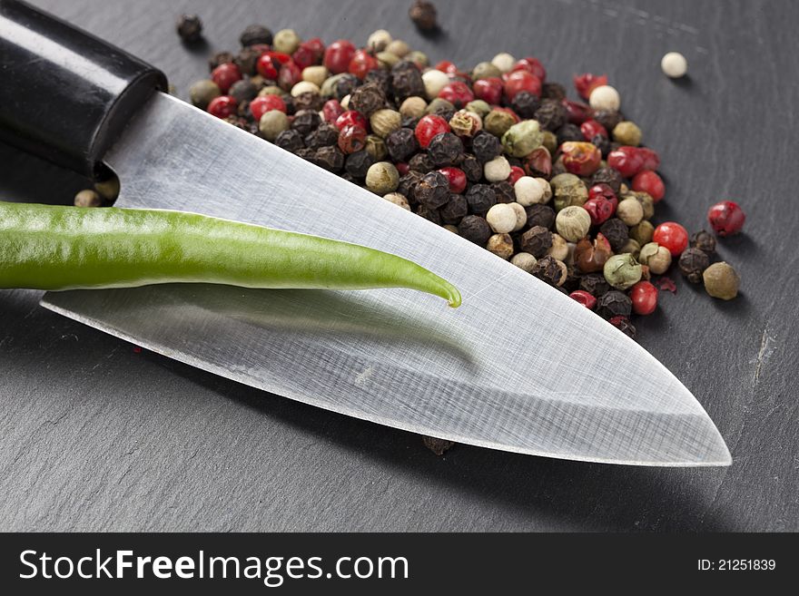 A knife, pepper and chili on a plate made of stone. A knife, pepper and chili on a plate made of stone