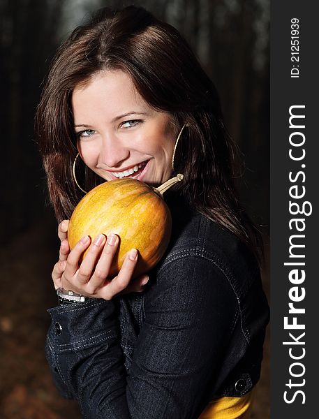Smiling brunette girl with pumpkin in dark forest. Smiling brunette girl with pumpkin in dark forest