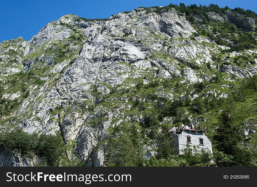 An old, ruined house in front of a huge rock wall. An old, ruined house in front of a huge rock wall