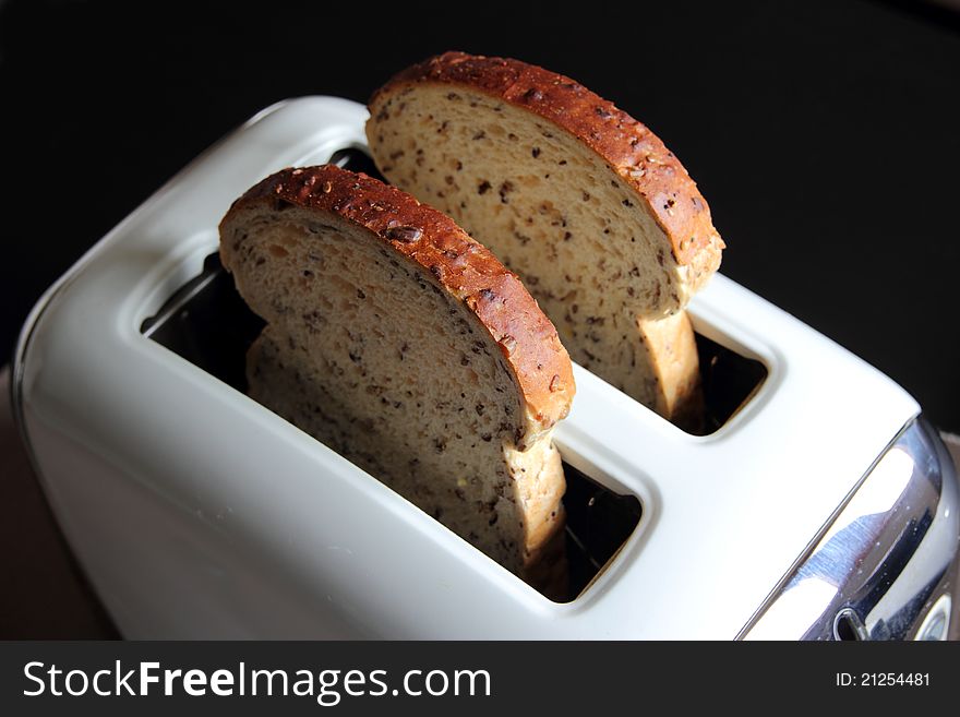 Two slices of bread in toaster, window-lit, shot against dark background. Two slices of bread in toaster, window-lit, shot against dark background