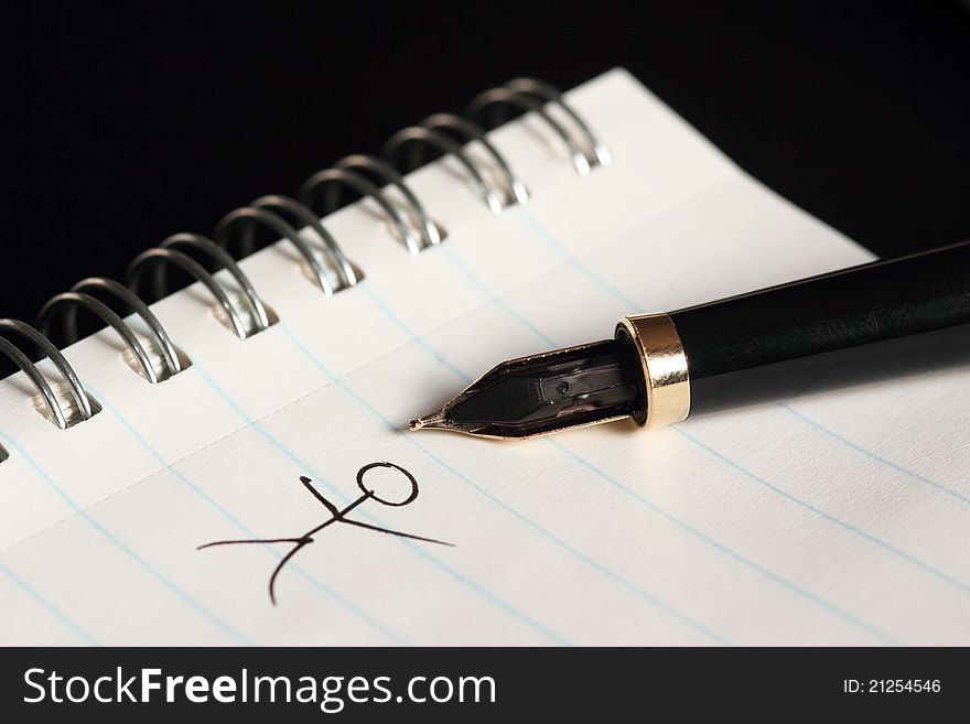 Fountain pen resting on pad of paper, with image of stick figure drawn on pad. Fountain pen resting on pad of paper, with image of stick figure drawn on pad