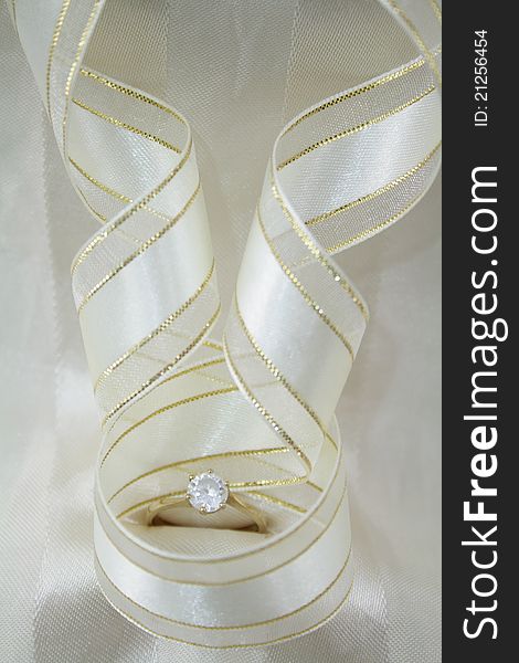 Diamond ring with gold and cream ribbon on cream satin background.