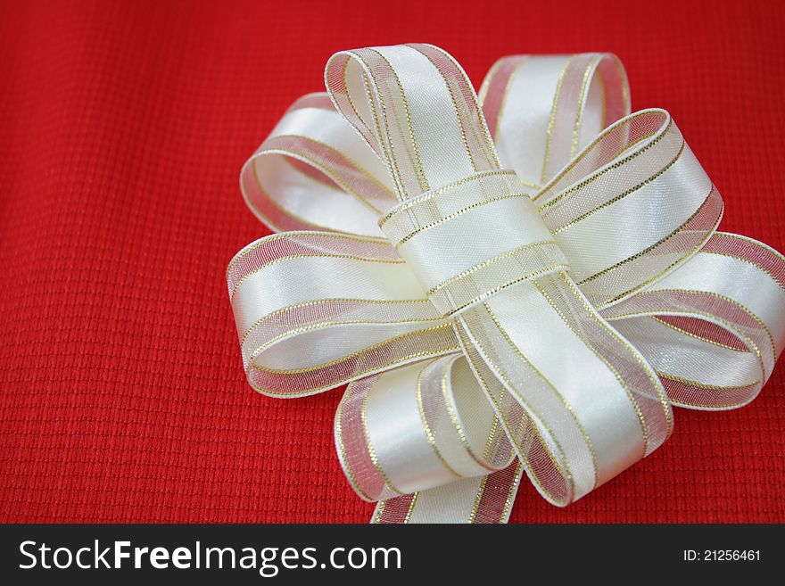 Cream and gold ribbon flower on red background.