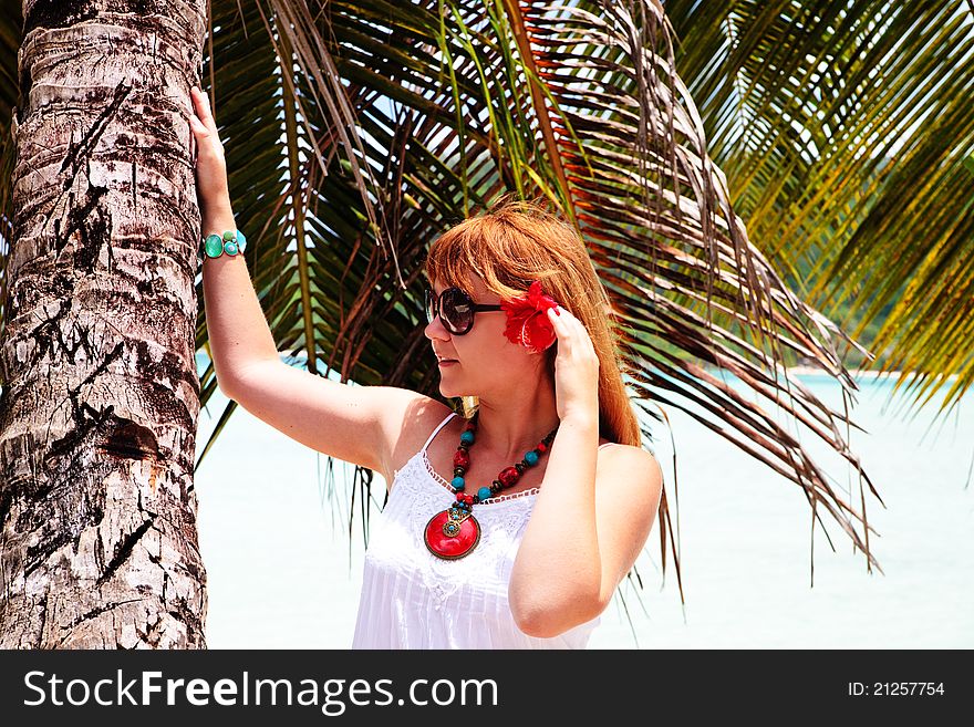 Beautiful woman with red flower in her hair stand under palm tree. Beautiful woman with red flower in her hair stand under palm tree