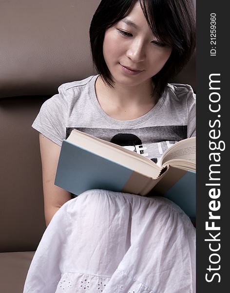 Young Woman Sitting On Sofa Reading Book