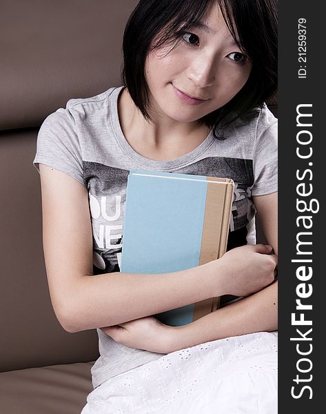 Thinking beautiful girl with the book sitting on sofa