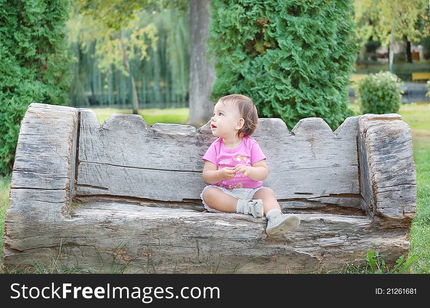 Little cute girl sitting on a bench in a park. Little cute girl sitting on a bench in a park.