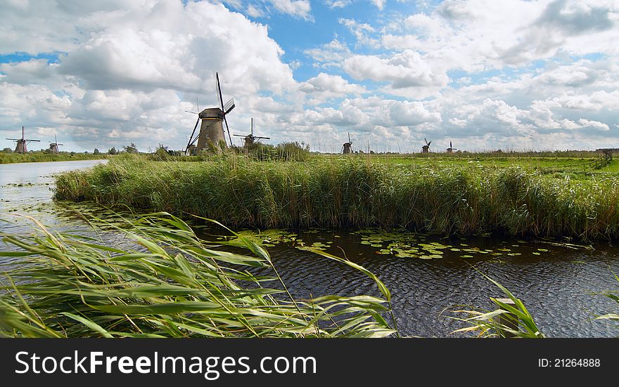 Windmill along a small canal against the background of cloudy sky. Windmill along a small canal against the background of cloudy sky