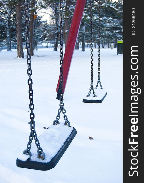 Empty children swings construction in a winter, snowy park. Empty children swings construction in a winter, snowy park