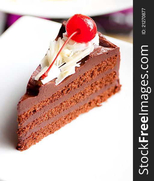 A soft chocolate cake with cherry on white dish