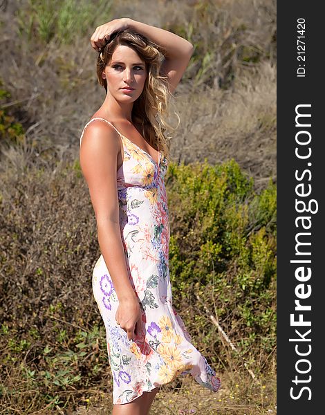 Blonde model in floral dress in field of grasses looking off in the distance