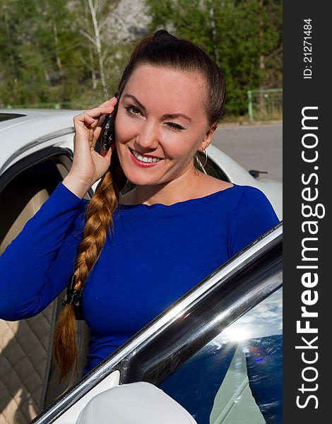 Woman winking and smiling with a cell phone in the street near the car. Woman winking and smiling with a cell phone in the street near the car