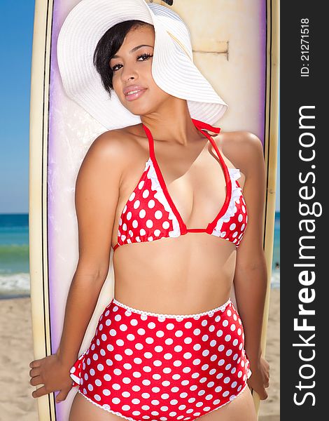 Model wearing white floppy hat in red polka-dot bikini and holding surfboard. Model wearing white floppy hat in red polka-dot bikini and holding surfboard