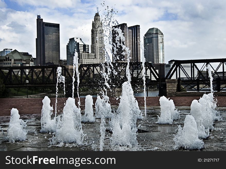 A photo of a fountain with a city scape in the background. A photo of a fountain with a city scape in the background.