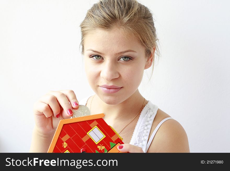 teenage girl putting a big silver coin in her moneybox looking at the camera. teenage girl putting a big silver coin in her moneybox looking at the camera